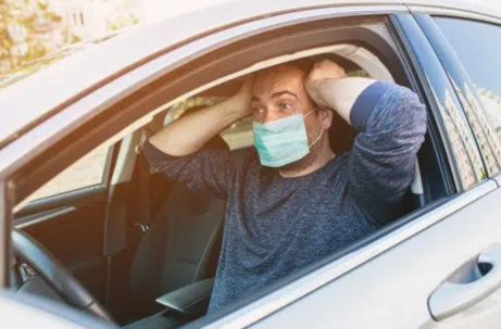 Man with his hands on his head while driving in his car with a mask on